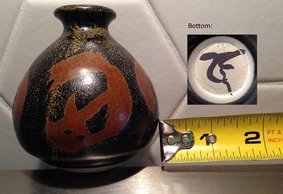 Small Japanese looking stoneware art studio pot with narrow neck and bulbous shape with red kanji characters on the black ground with brown speckle decoration and a black kanji pottery marking
